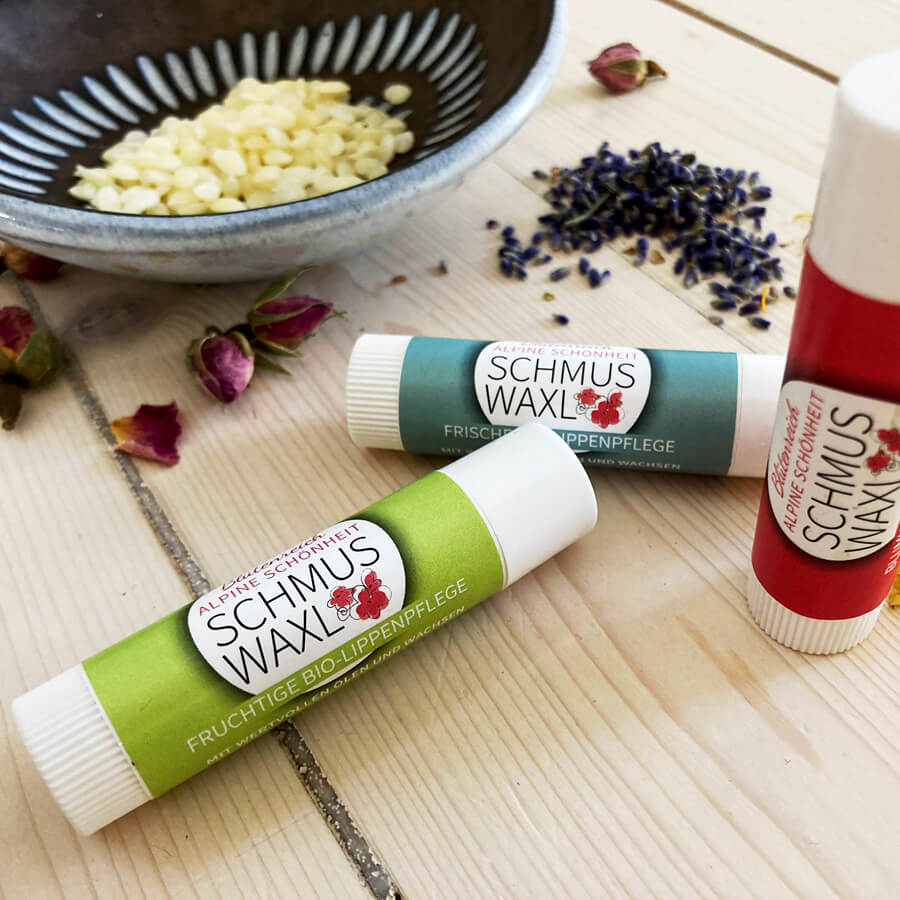 Drei Bio Lippenbalsam Schmus Waxl fruchtig frisch und blumig, Bienenwachs in grauem Schüsselchen, Rosenblätter, Lavendel